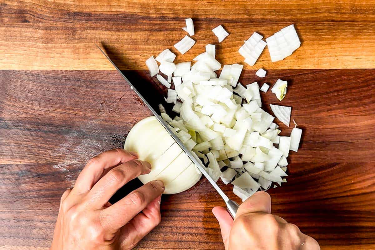 Dicing up an onion with a chef's knife on a wood cutting board.