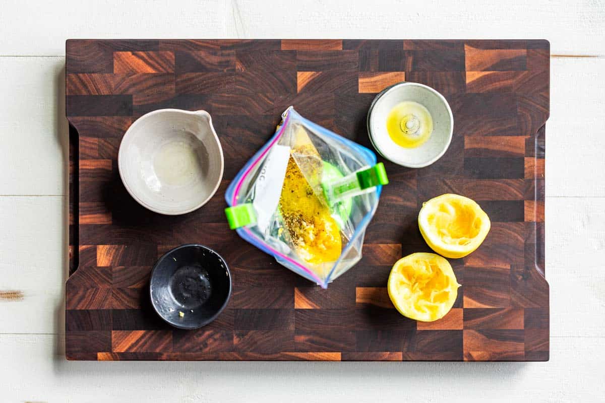 Lemons, oregano, and olive oil in bowls on a wood cutting board.