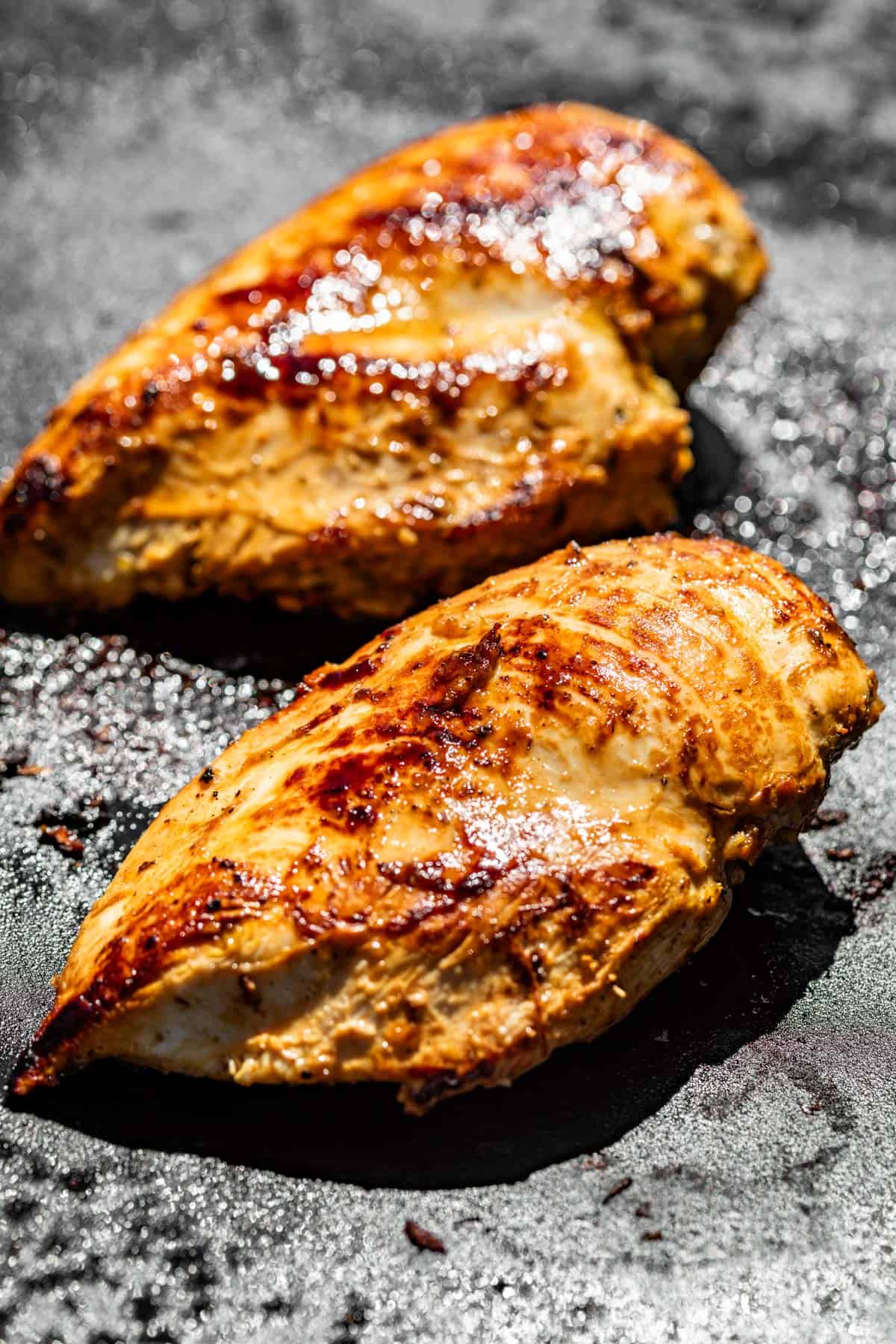 Two chicken breasts cooking on a griddle.