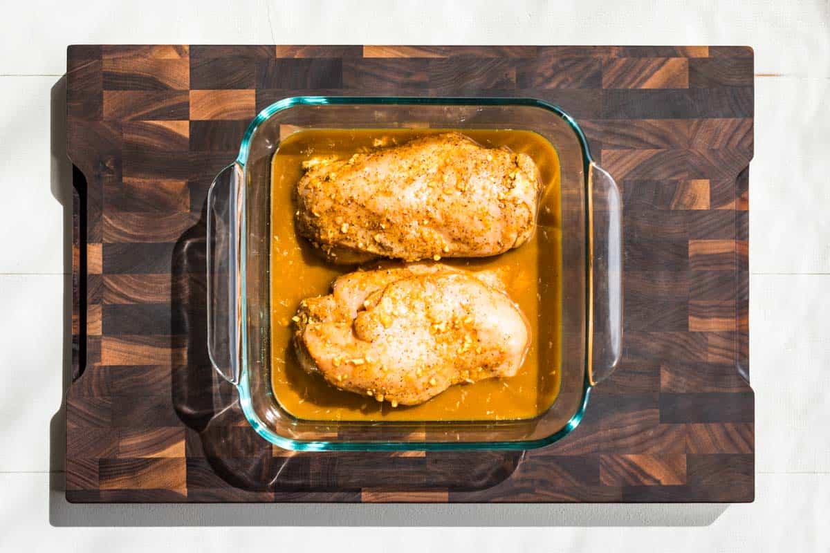 Baked 5-Spice Orange Chicken Marinade in a square glass dish on a wooden cutting board.