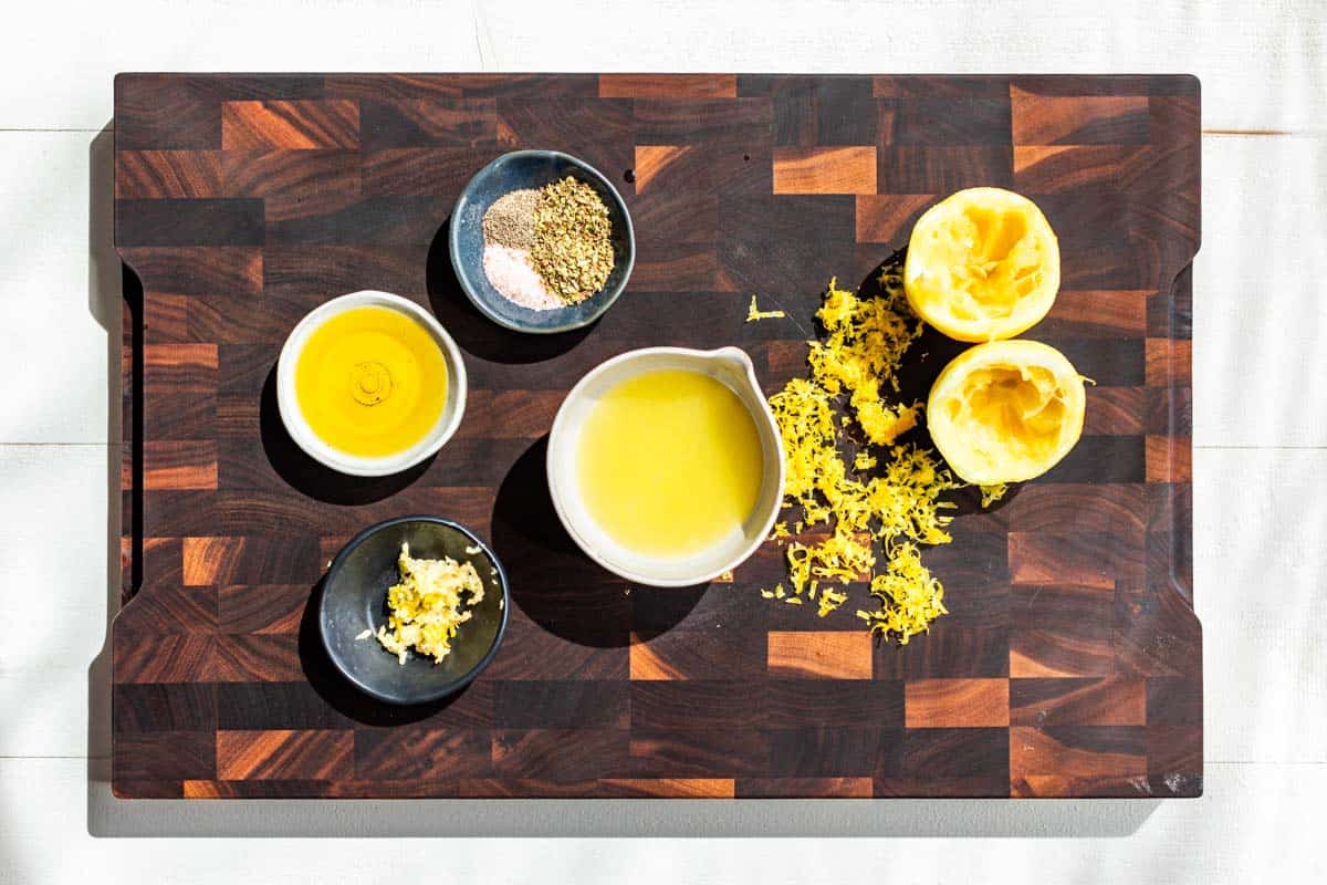 All the ingredients for the Greek Chicken Marinade measured out in small bowls on a wooden cutting board.