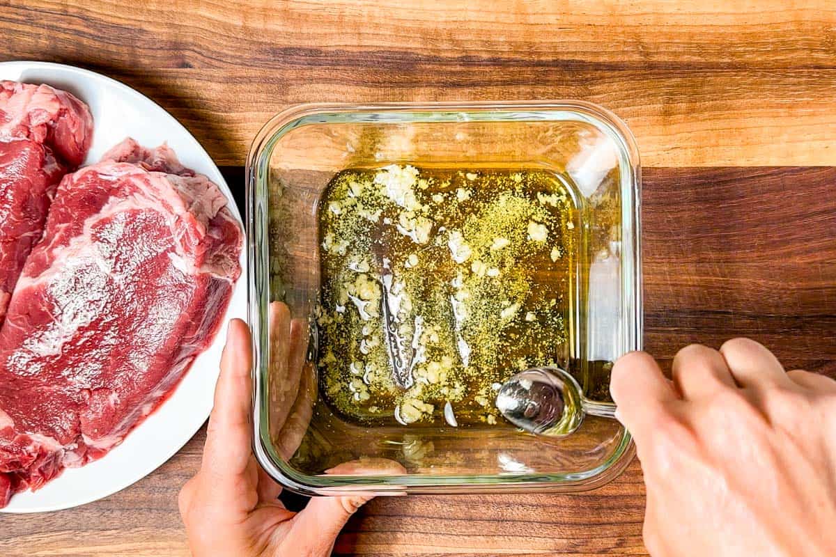 Stirring together minced garlic, olive oil, and salt in a glass container to make a marinade.