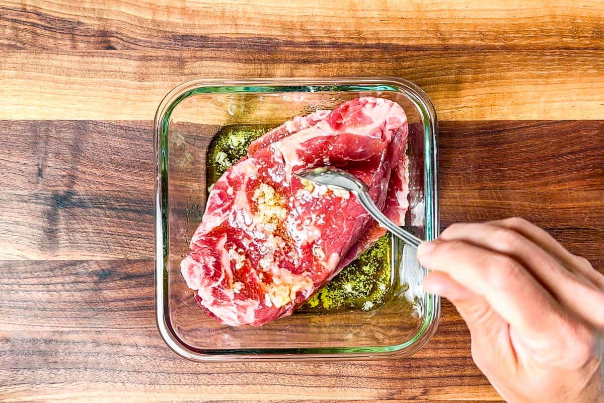 Coating the steaks with the garlic olive oil marinade in a glass dish.