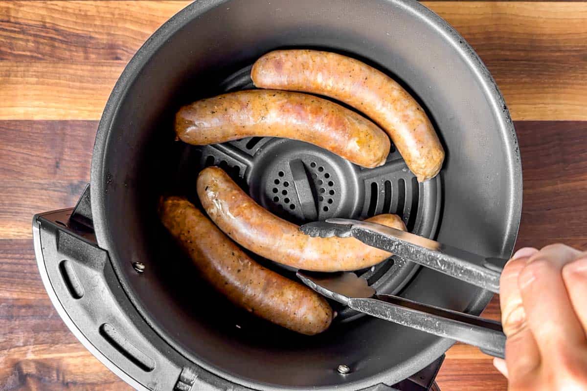 Turning the Italian sausages over halfway through the cooking time with a pair of tongs.
