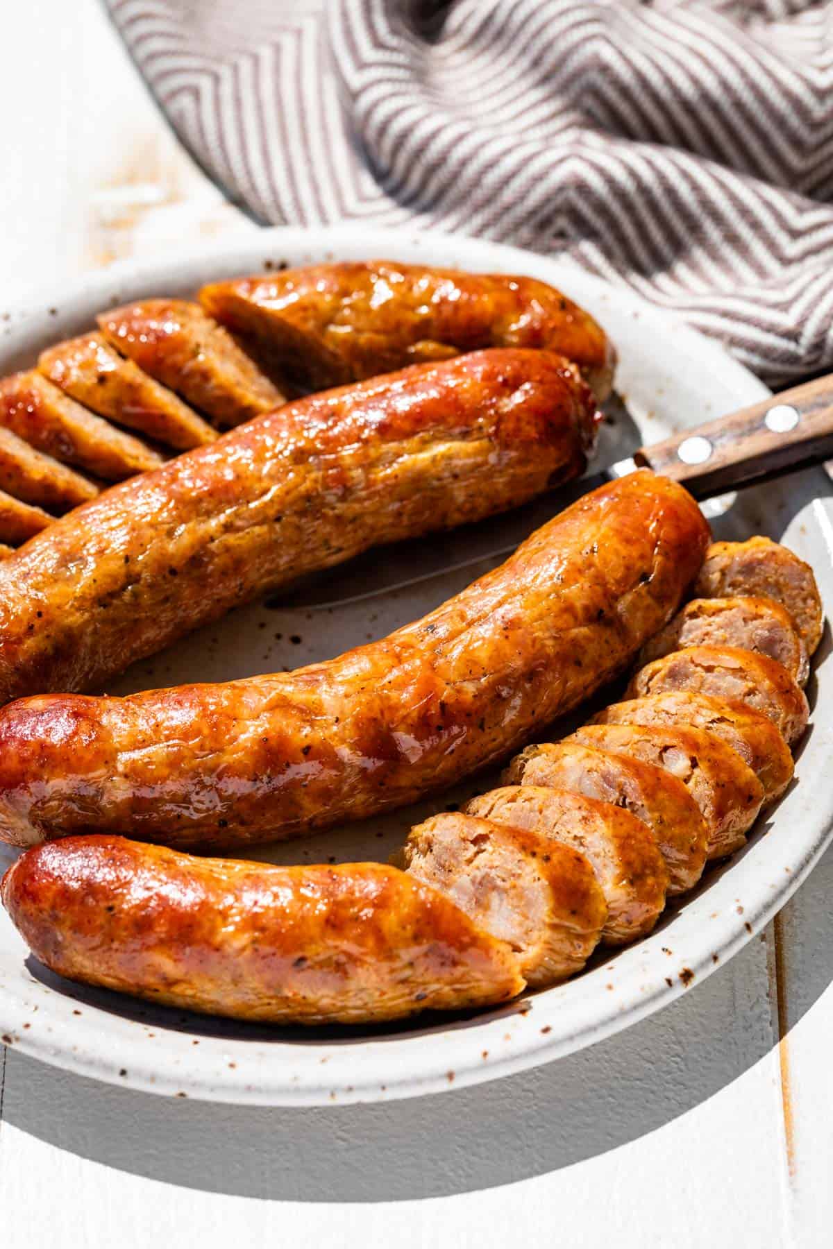 Four sliced browned Italian sausages on a pottery plate with a brown linen on the side of the plate.