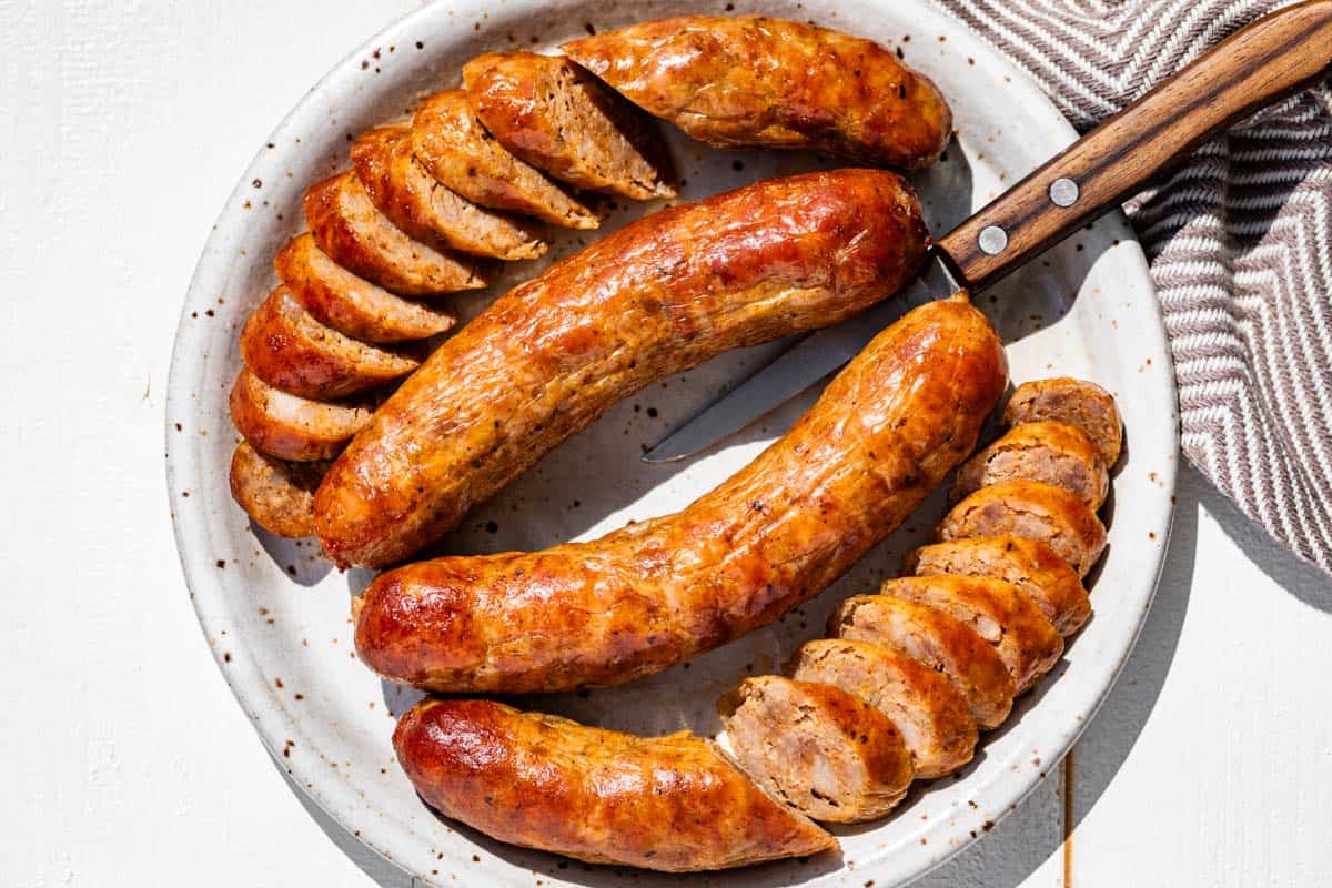 Finished Italian sausage on a pottery plate with two sausages partially sliced.