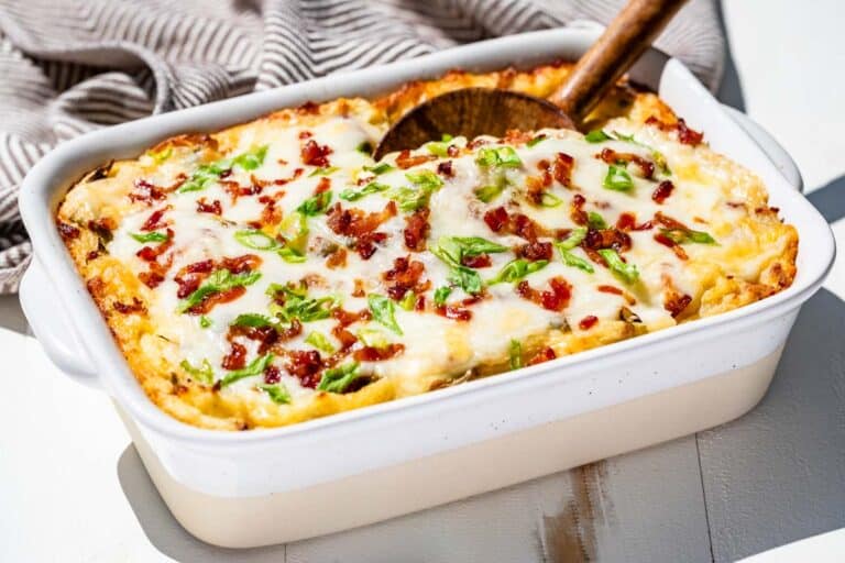 Baked cheesy mashed potatoes in a pottery baking dish with a wood spoon scooping some out.