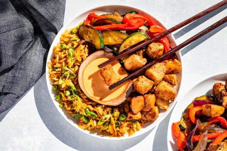 Hibachi chicken, hibachi vegetables, and hibachi fried rice on a white plate with a small bowl of yum yum sauce and chopsticks dipping a piece of chicken into the sauce.