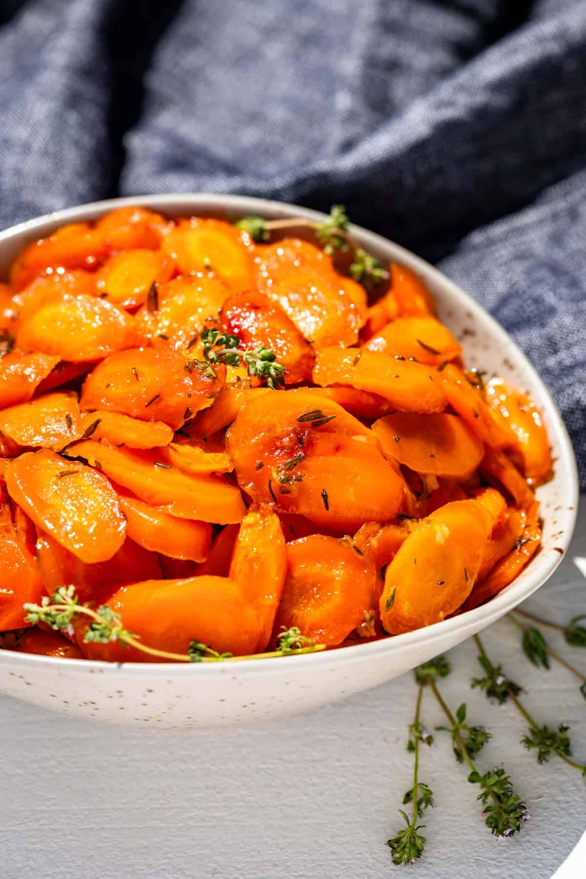 Honey glazed carrots in a taupe pottery serving bowl topped with sprigs of thyme on top and the side of the bowl.