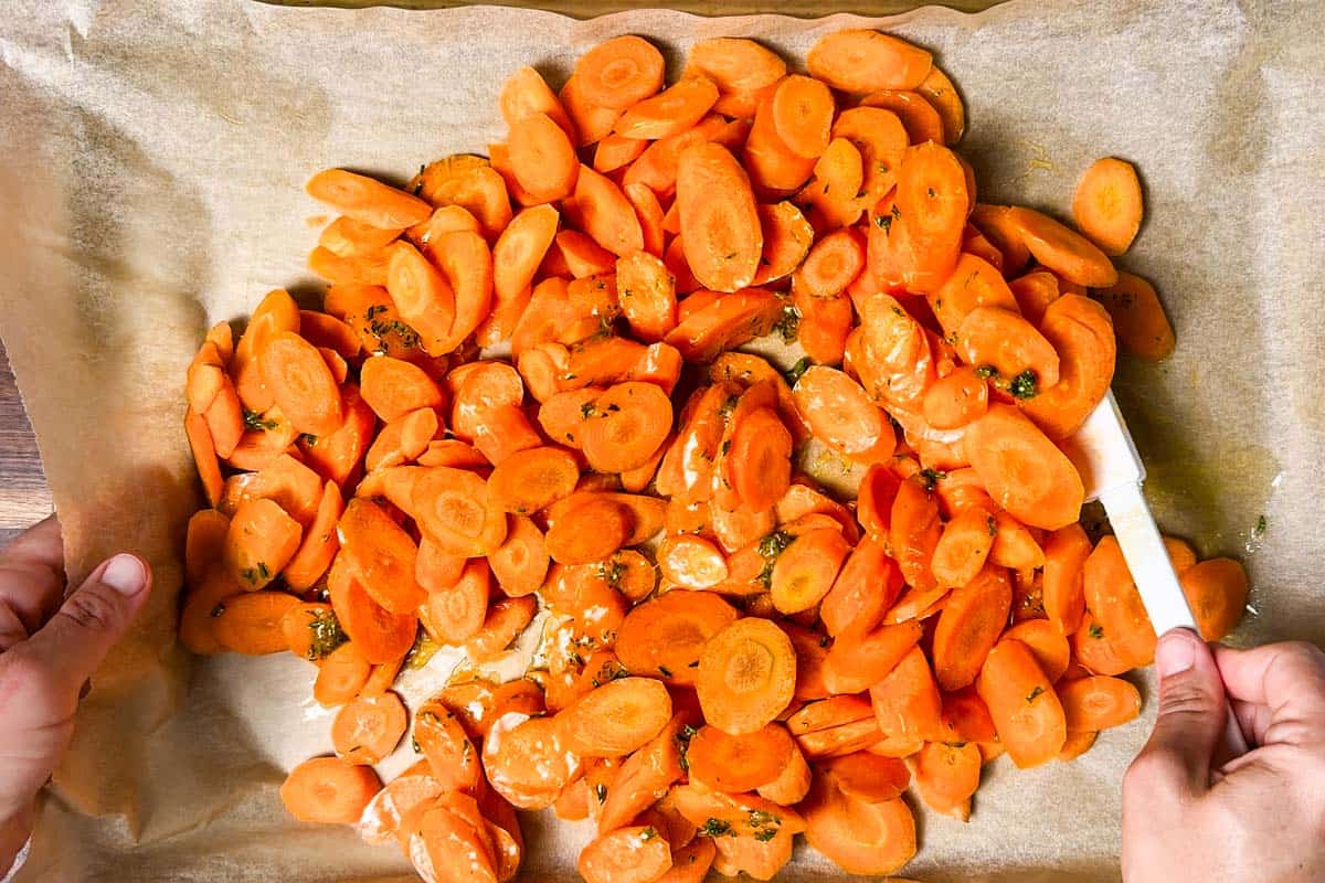 Tossing the sliced carrots together with the honey butter mixture on a parchment lined baking sheet.