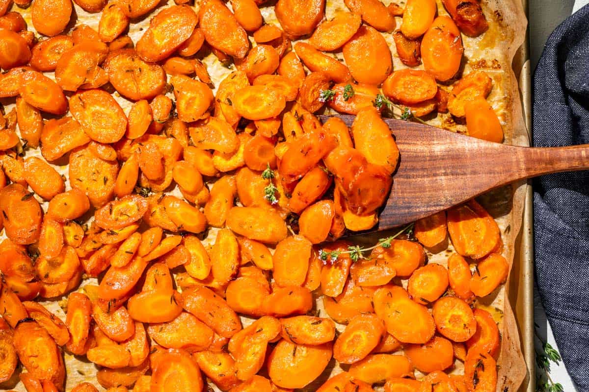 Roasted Honey Glazed Carrots on a gold baking sheet with a wood spatula scooping up some.