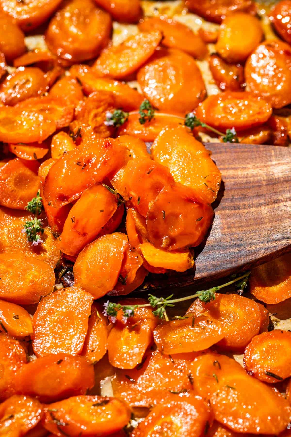 A wood spatula scooping up honey glazed carrots from a baking sheet pan.