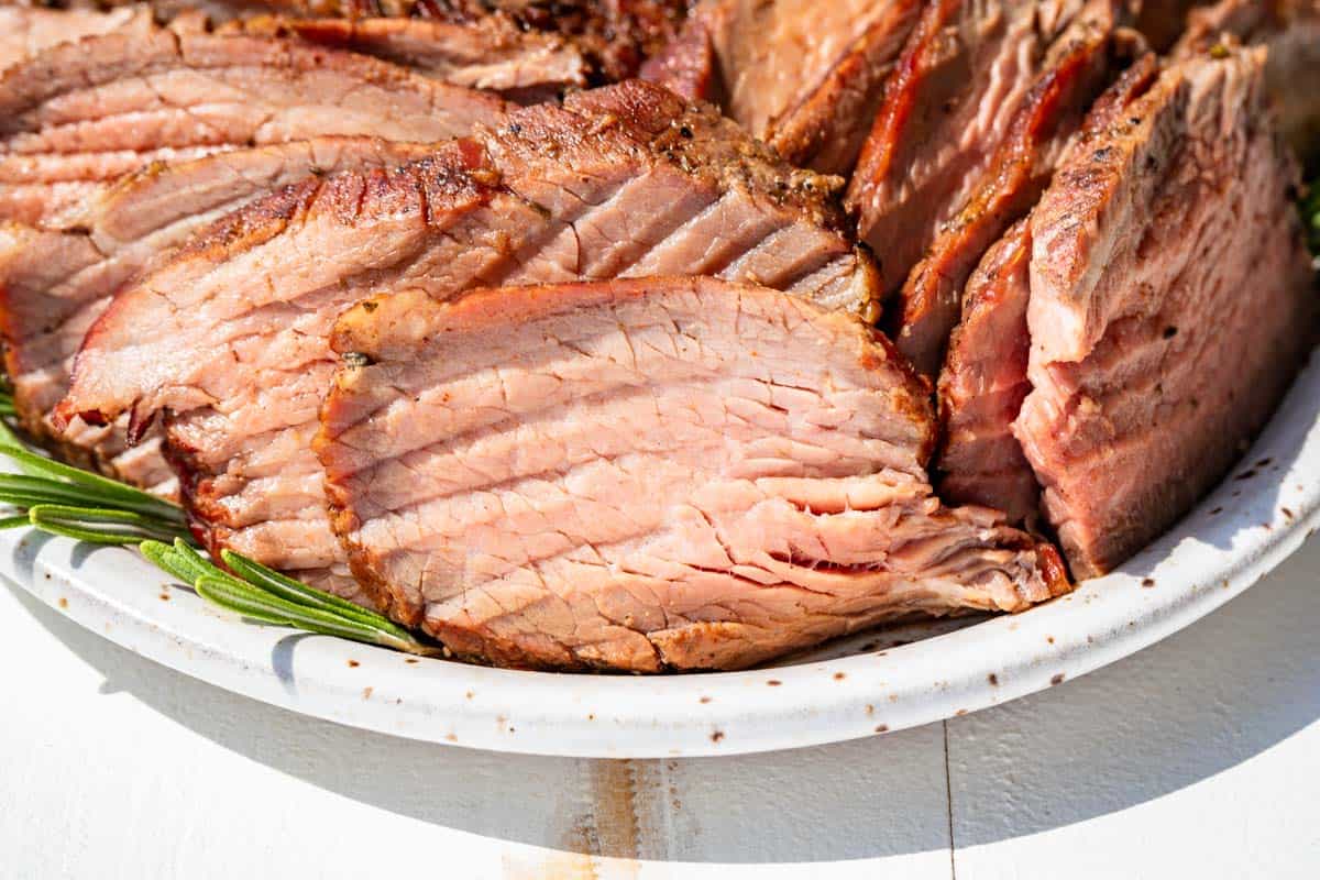Finished sliced smoked tri tip on a pottery plate with sprigs of rosemary on the side.