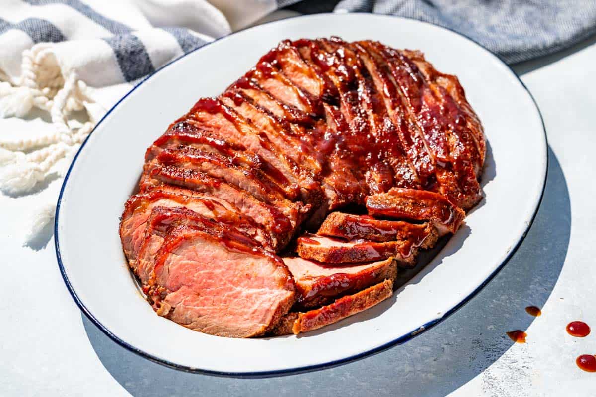 Sliced BBQ Smoked Tri Tip on a blue rimmed white oval platter.