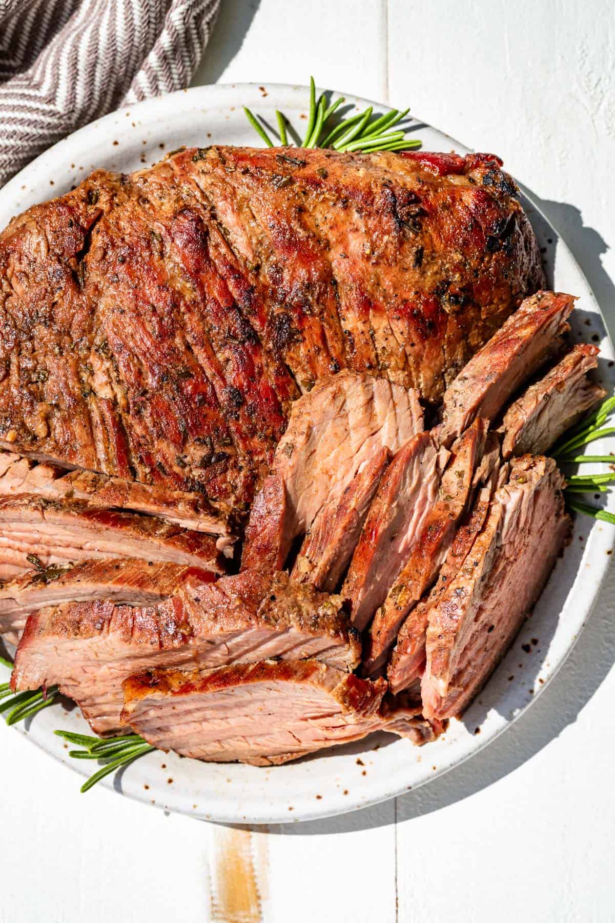 Finished smoked tri tip on a plate with rosemary sprigs on the side of the plate.