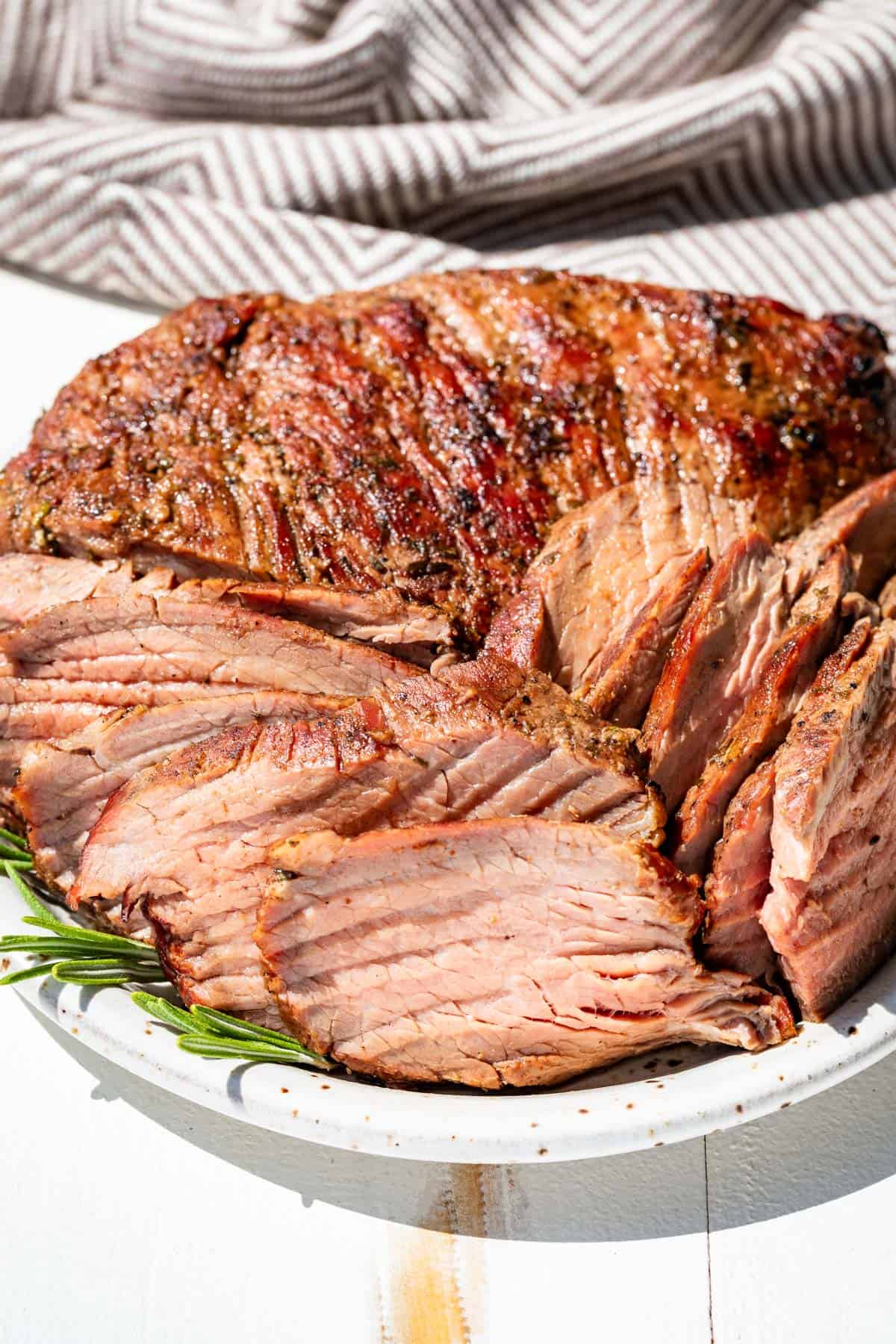 Sliced rosemary smoked tri tip on a speckled pottery plate with sprigs of rosemary on the side.
