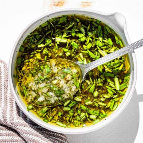 Mixing together the rosemary, olive oil, minced garlic, sea salt, and pepper in a small pottery bowl with a spout.