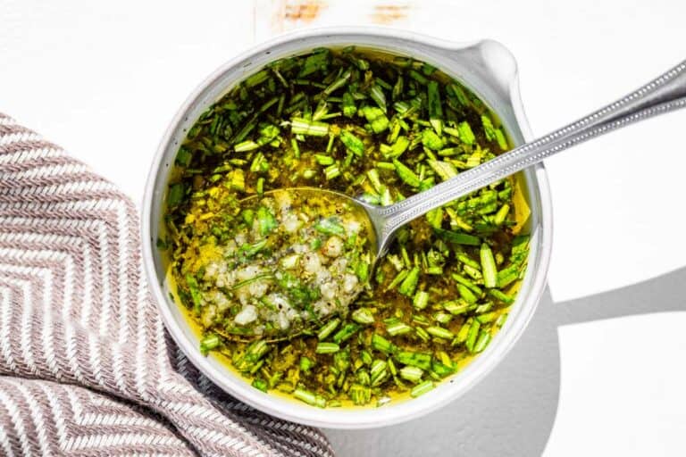 Mixing together the rosemary, olive oil, minced garlic, sea salt, and pepper in a small pottery bowl with a spout.