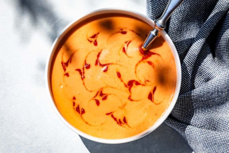 Finished Yum Yum Sauce in a white bowl topped with swirls of sriracha and a metal spoon in the bowl.