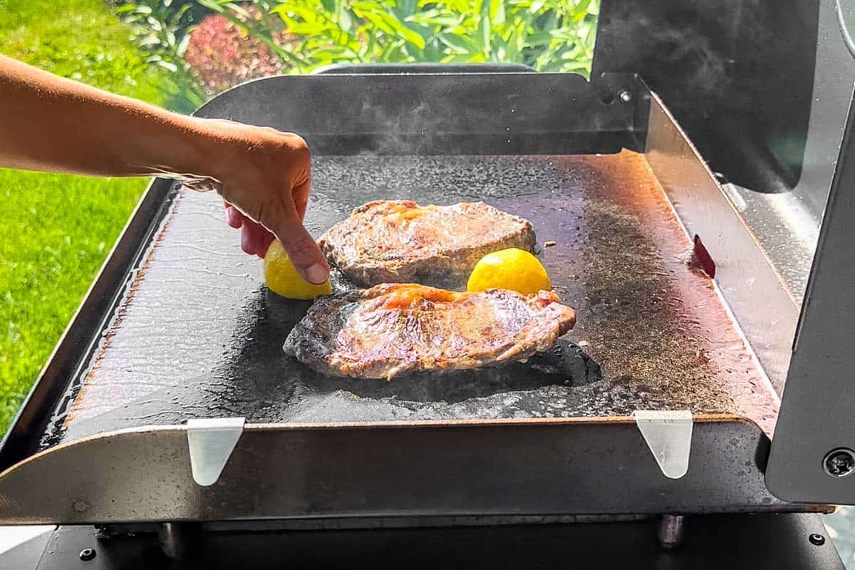 Adding lemon wedges to the griddle next to the steaks.