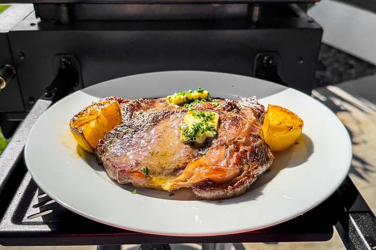 Topping the finished steaks with butter and chopped parsley on a white plate with lemon wedges on the side.