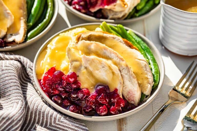 Gluten Free gravy poured over sliced turkey breast on a plate with mashed potatoes, cranberry sauce, and green beans.