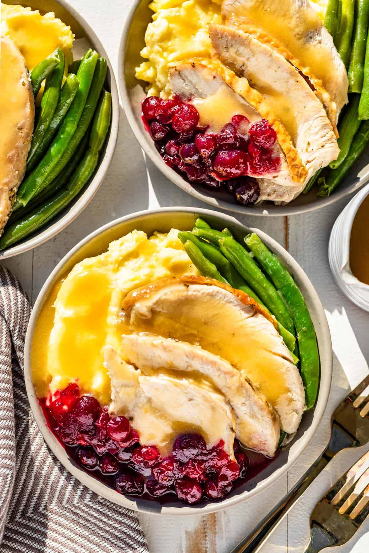 Gluten Free gravy poured over sliced turkey breast on a plate with mashed potatoes, cranberry sauce, and green beans.