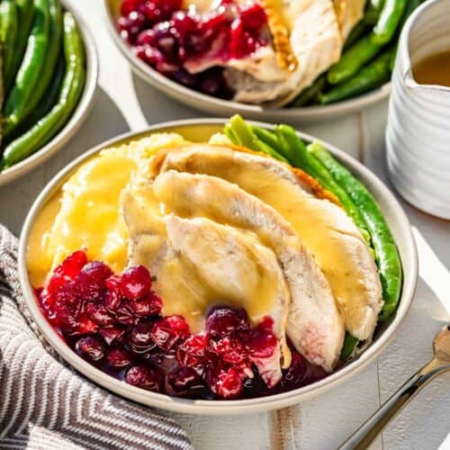 Gluten Free gravy poured over sliced turkey breast on a plate with mashed potatoes, cranberry sauce, and green beans.