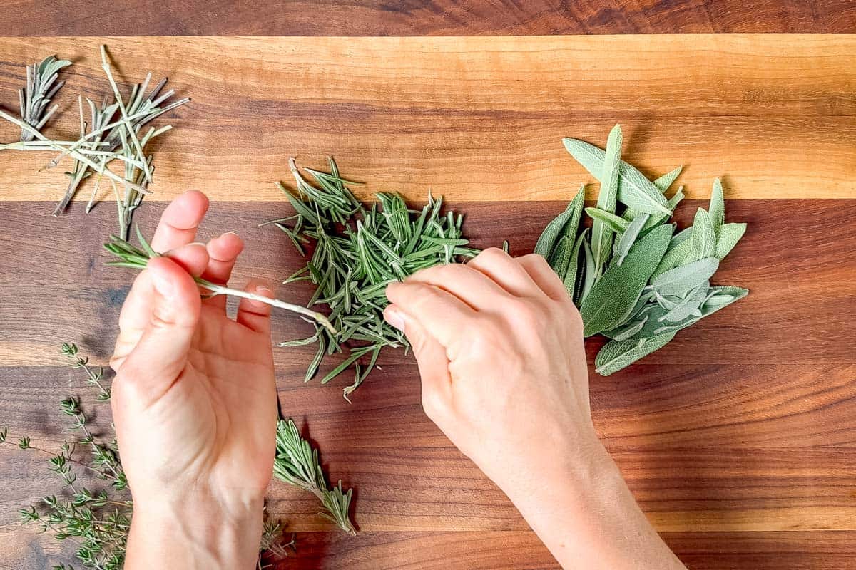 Removing the tough woody stems from the fresh herbs on a wood cutting board.