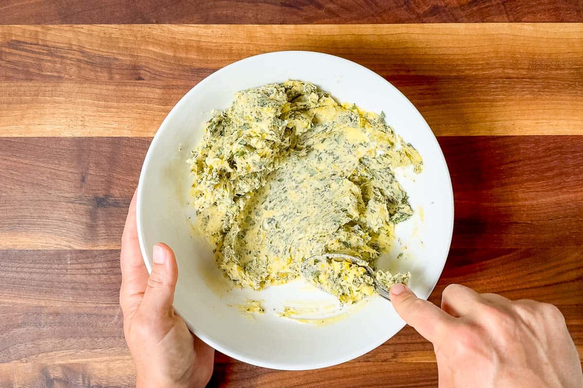 Mashing the lemon zest and chopped herbs into the butter in a large white bowl.