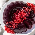 A molded cranberry pomegranate jello ring on a white plate topped with pomegranate arils and cranberries.