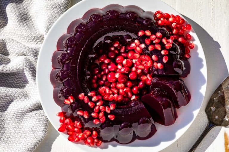 A molded cranberry pomegranate jello ring on a white plate topped with pomegranate arils and cranberries.