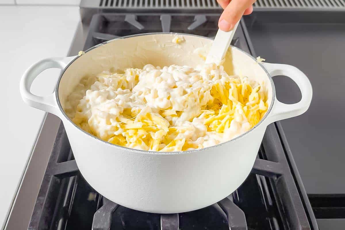 Stirring the elbow macaroni and cheese into the half and half mixture in a large white pot.