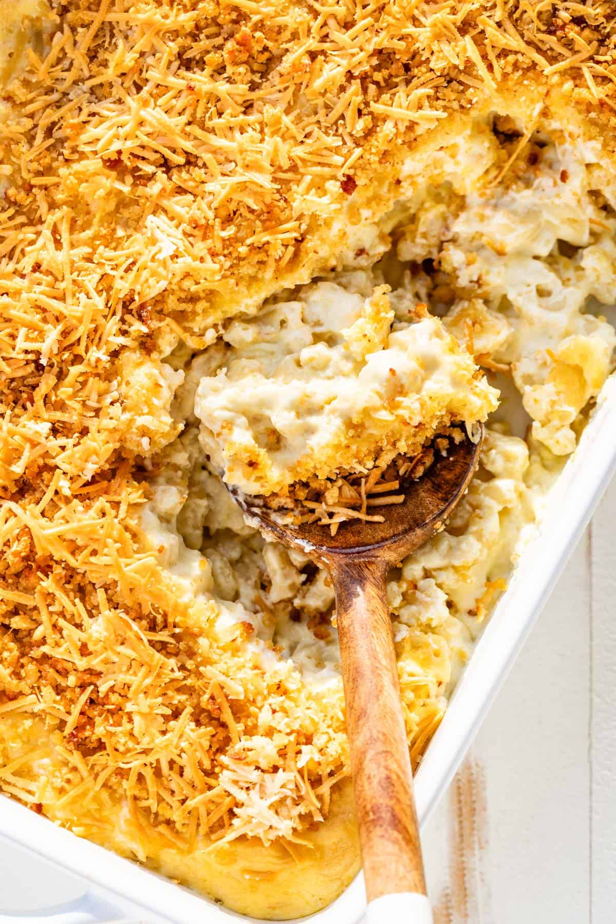 A large white baking dish with smoked mac and cheese topped with golden brown breadcrumbs and a wood spoon scooping some out.