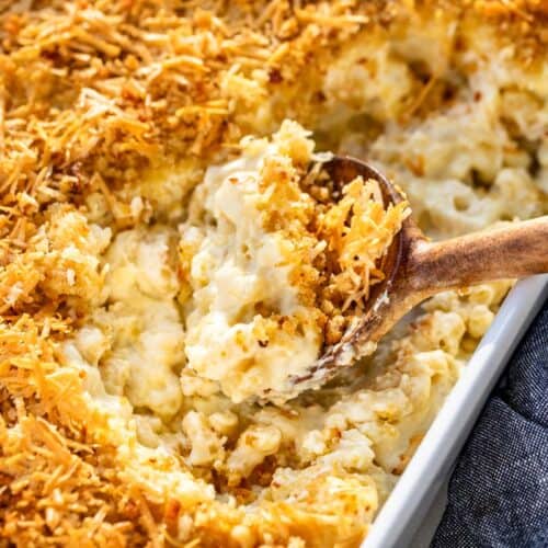 A wood spoon scooping out smoked mac and cheese from a white baking dish.