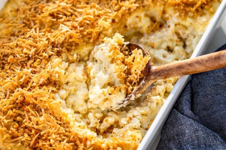 A wood spoon scooping out smoked mac and cheese from a white baking dish.