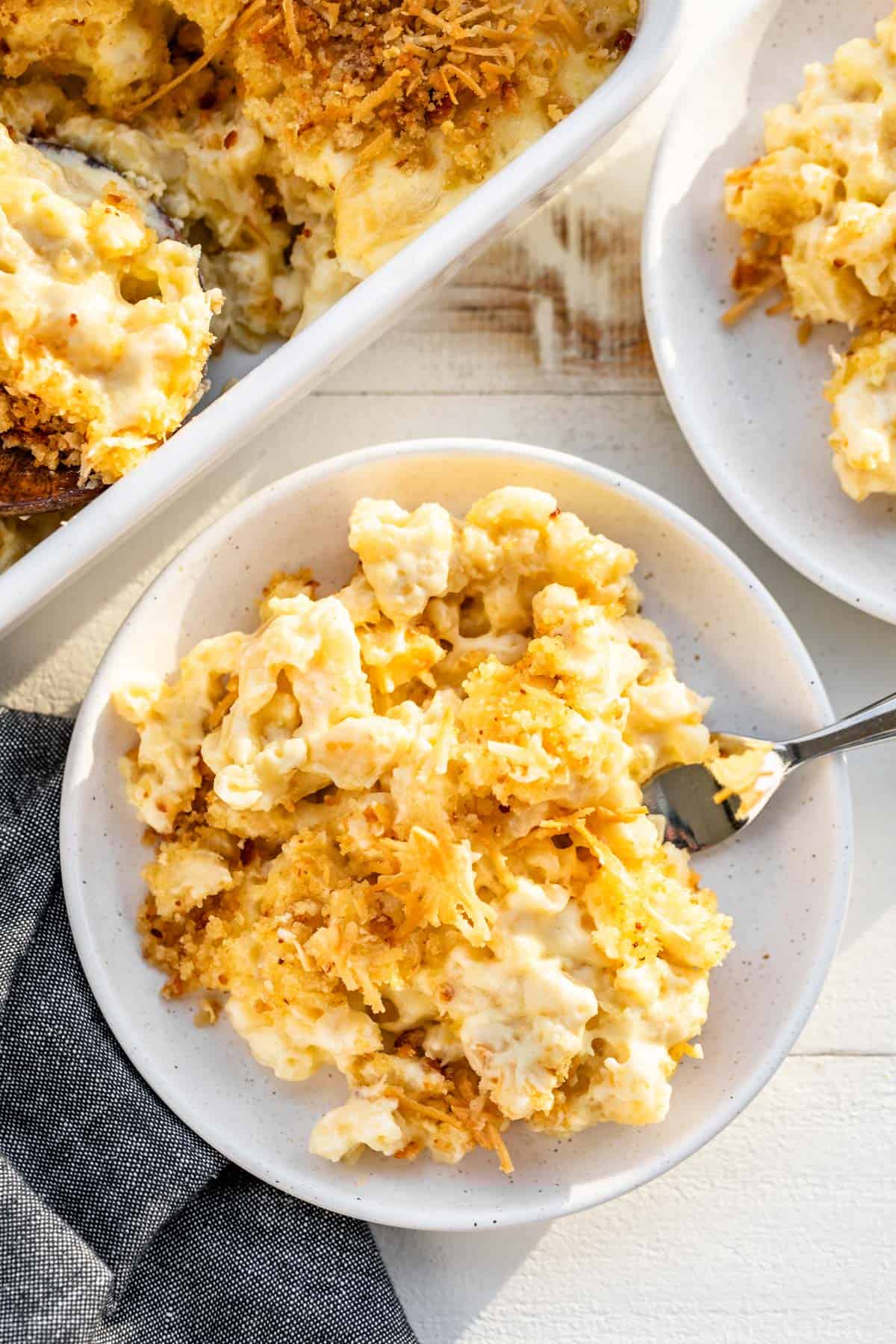 Two plates of smoked mac and cheese with a fork on the side of one plate and a baking dish of mac and cheese on the side.