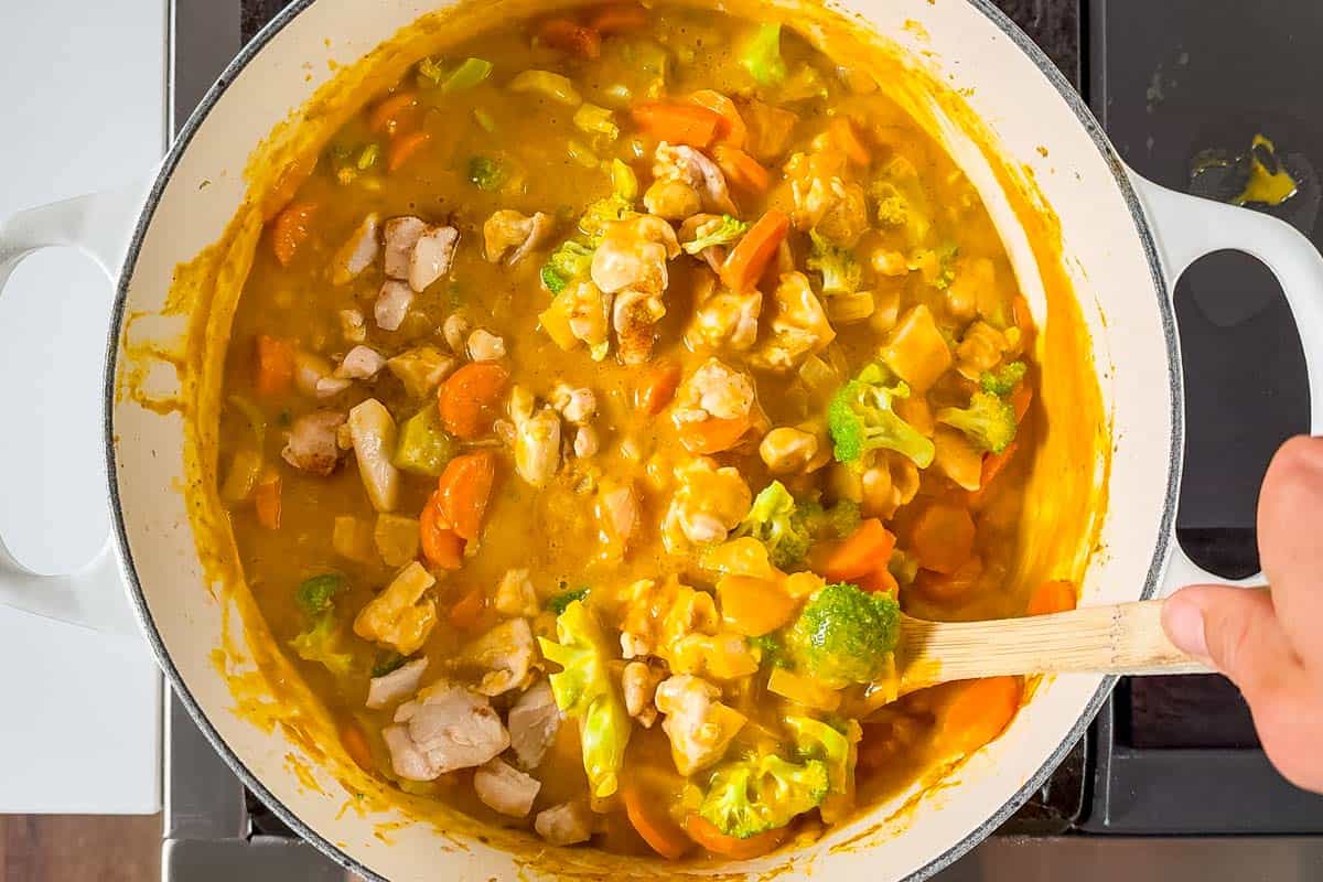 Adding the broccoli florets to the finished pumpkin curry and stirring with a wood spoon.