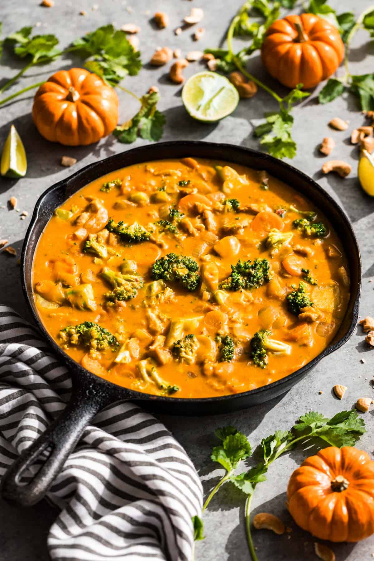 Thai pumpkin curry in a black cast iron skillet with a black and white linen on the side of the skillet surrounded by mini pumpkins and limes.