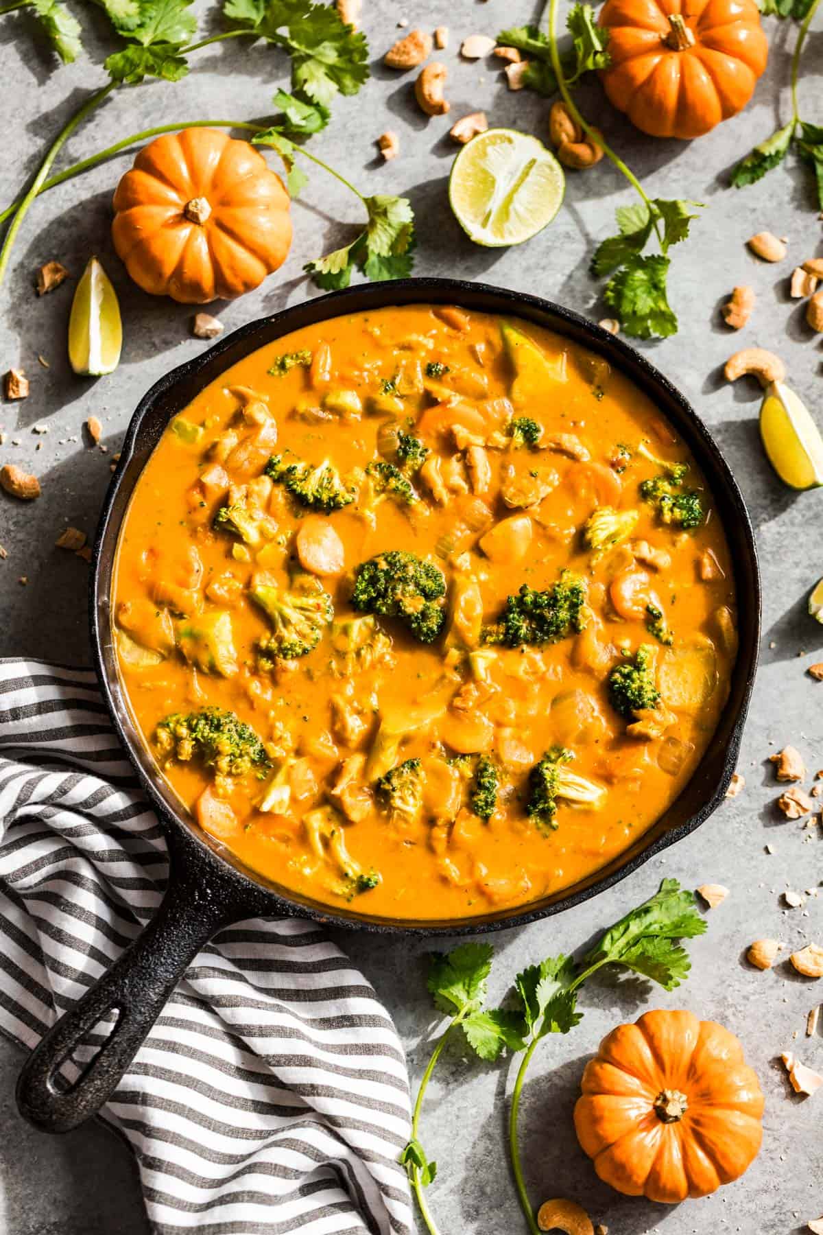 Pumpkin curry in a cast iron skillet with mini pumpkin and cilantro around the skillet.