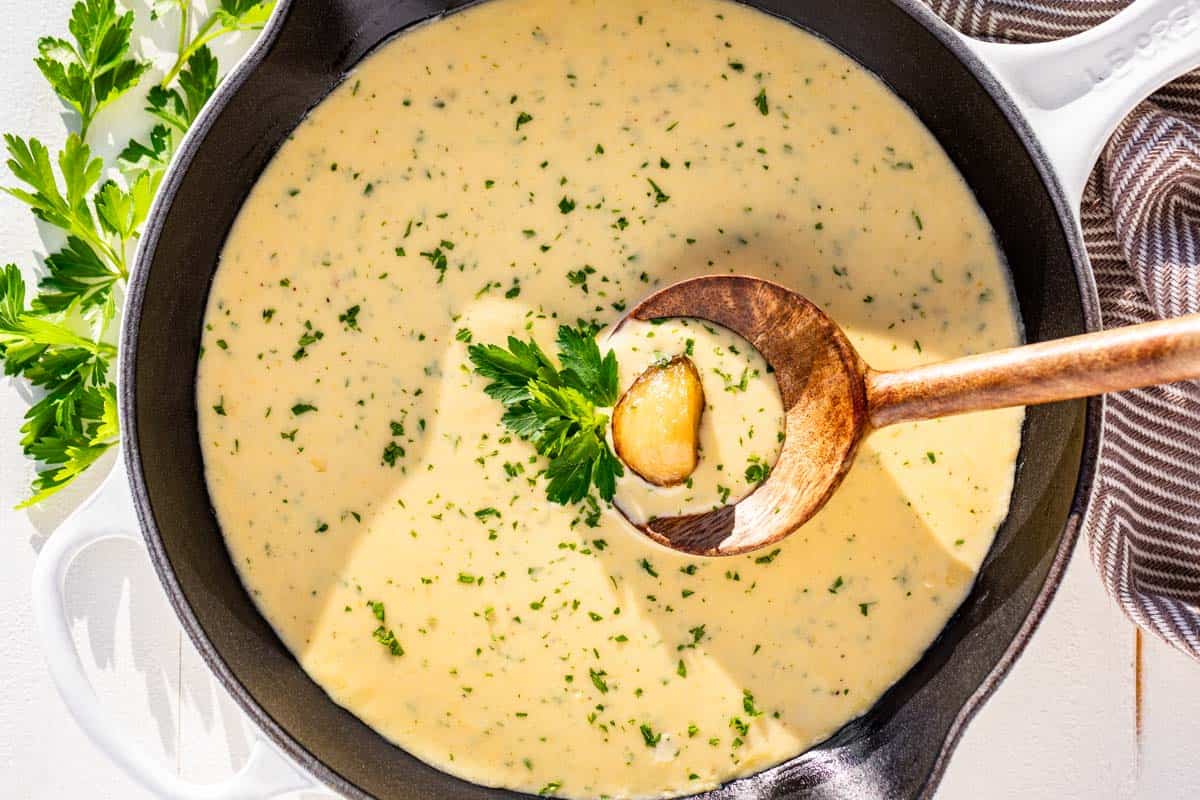 Finished garlic cream sauce in a white cast iron skillet garnished with a clove of roasted garlic and topped with parsley.