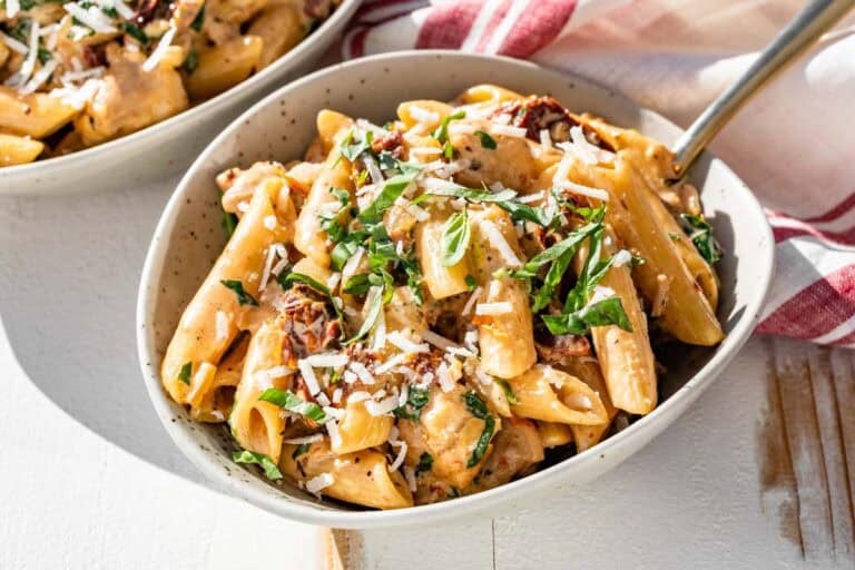 Two bowls filled with Marry Me Chicken Pasta with a gold fork in one and a red and white linen in the background.