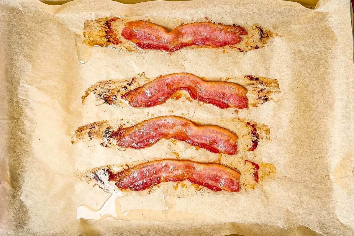 Par-baked bacon strips on a parchment lined baking sheet.