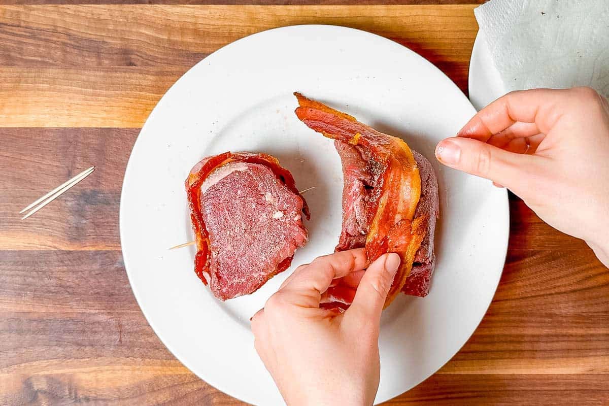 Wrapped the seasoned filet mignon steaks with the par-baked bacon and securing the ends with a toothpick.