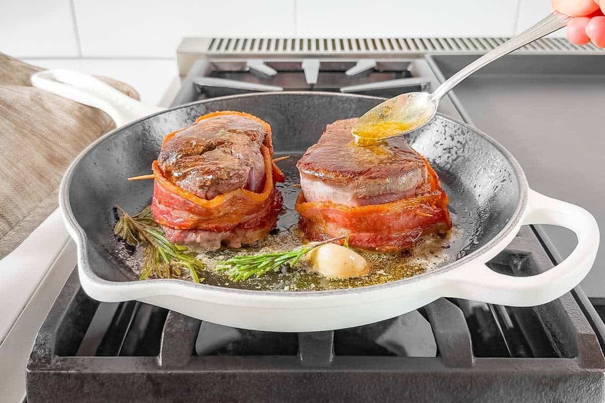 Butter basting the bacon wrapped filet mignon steaks in a cast iron skillet on the stovetop.