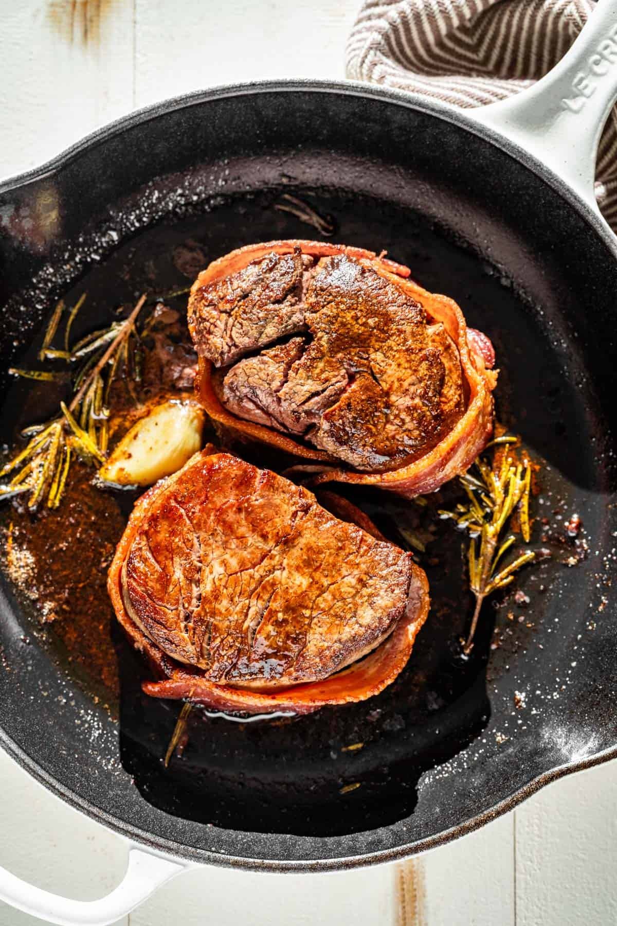 Two bacon wrapped filet mignon steaks in a white cast iron skillet.