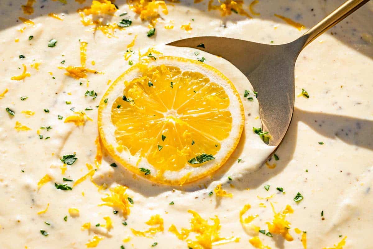 Close view of lemon cream sauce topped with a slice of lemon, lemon zest, and chopped parsley.