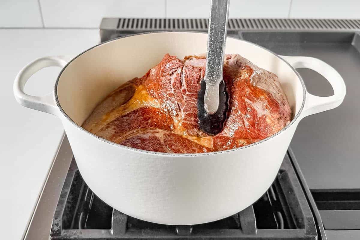 Searing the chuck roast in a large white Dutch oven on the stove top.