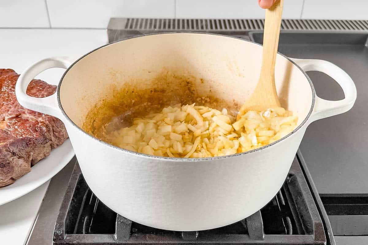 Sautéing onions and garlic in a white Dutch oven.
