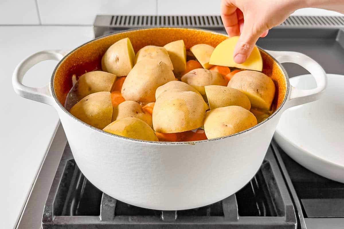Adding the potatoes, carrots, and celery to the half cooked pot roast.